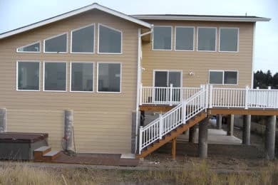 Tan two-story house on pilings with white-railed deck and hot tub in Moclips