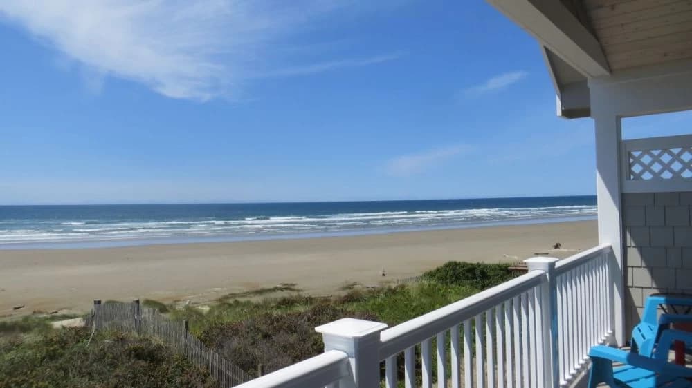 White deck railing in Florence overlooking dunes, a wide sandy beach, and blue ocean