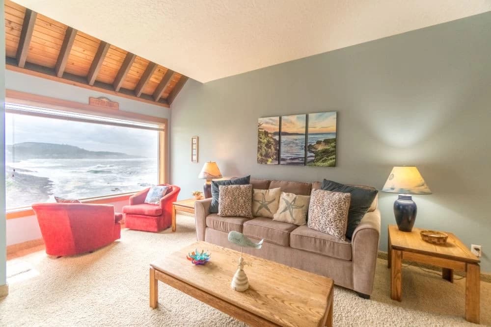 Tan sofa and red chairs face an ocean-view window in Depoe Bay