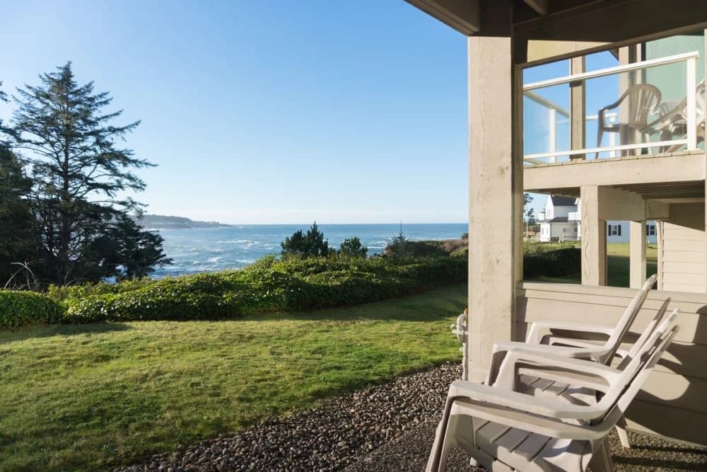 White patio chairs in Depoe Bay facing the ocean beside a tan house and lawn