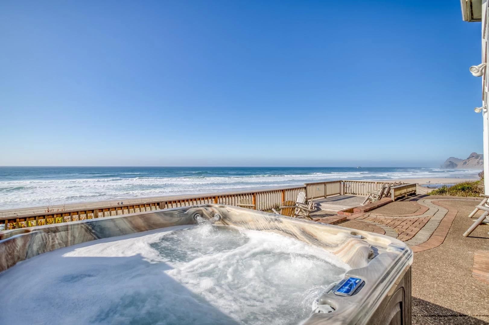 Bubbling hot tub in Lincoln City on a patio overlooking the beach, ocean, and wooden chairs
