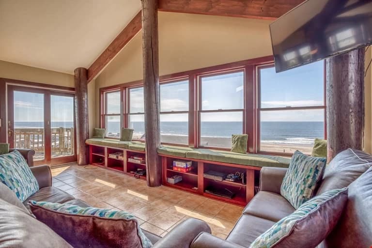 Brown leather sofas and log pillars face ocean-view windows in Lincoln City