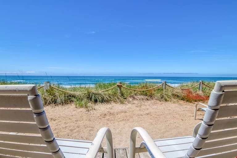 White lounge chairs on a sandy deck overlooking ocean and dunes in Neskowin