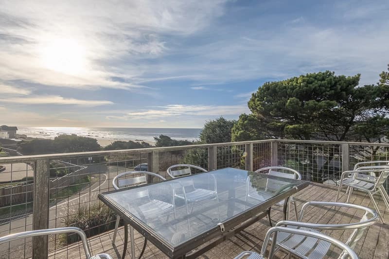 Glass dining table on a wooden deck overlooking trees and ocean in Lincoln City