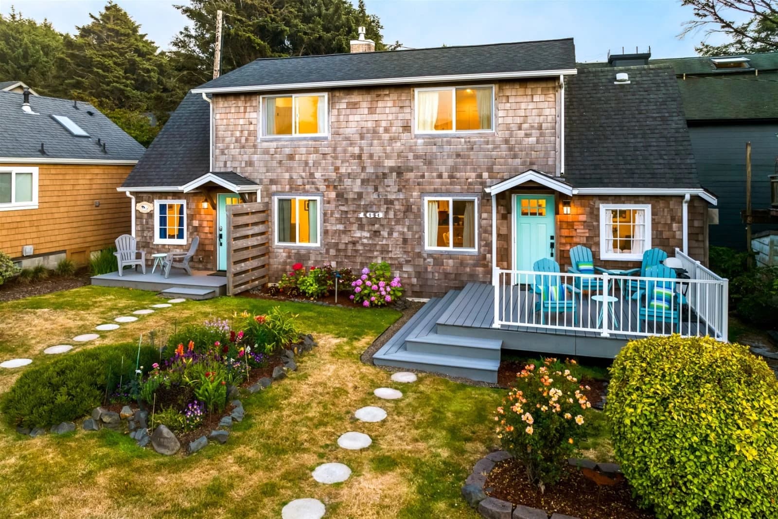 Gray-shingle duplex in Cannon Beach with turquoise doors, decks, and flower beds