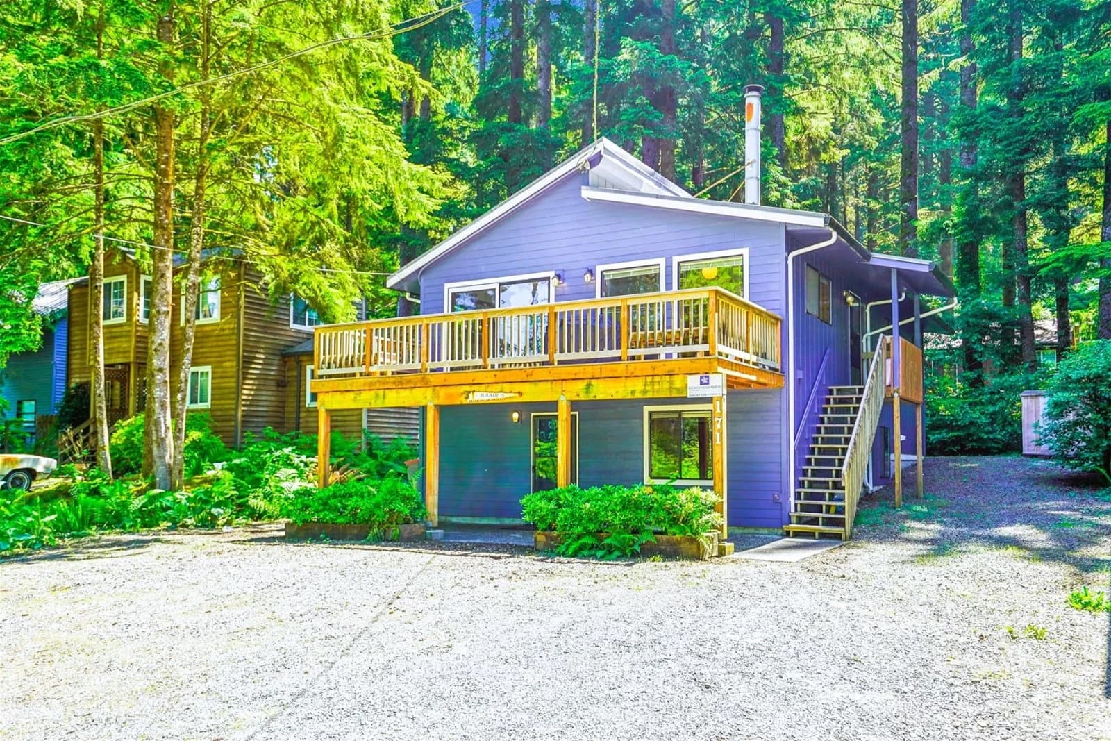 Lavender two-story house in Cannon Beach with a wood deck among evergreen trees