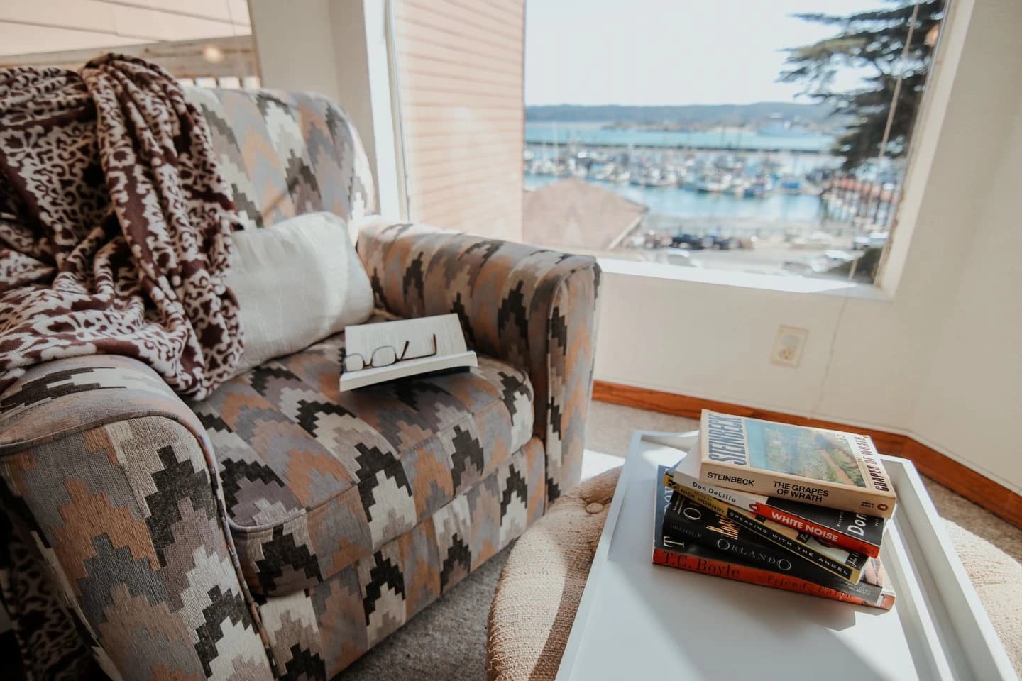 Patterned armchair and books by a window overlooking a marina of boats in Newport